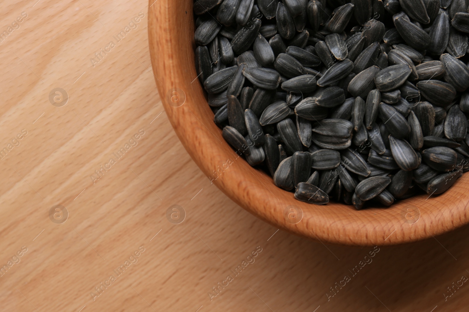 Photo of Organic sunflower seeds in bowl on wooden table, top view. Space for text