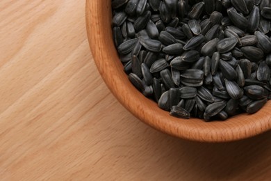 Organic sunflower seeds in bowl on wooden table, top view. Space for text