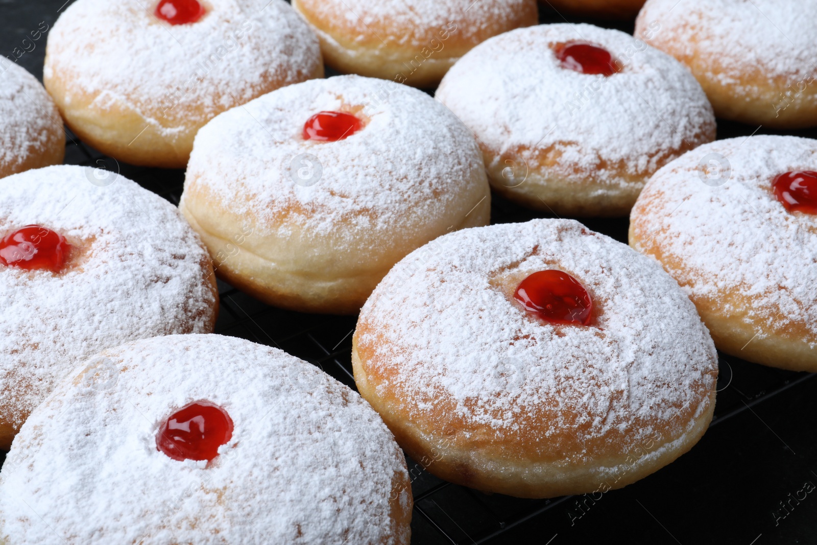 Photo of Many delicious donuts with jelly and powdered sugar on cooling rack, closeup