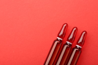 Glass ampoules with liquid on red background, top view. Space for text