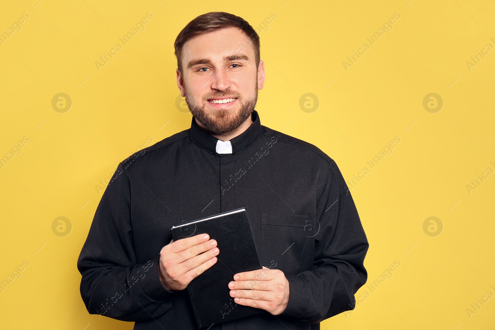 Photo of Priest in cassock with Bible on yellow background