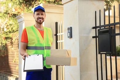 Courier in uniform holding order receipt and parcels outdoors