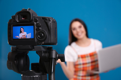 Young blogger with laptop recording video against blue background, focus on camera screen