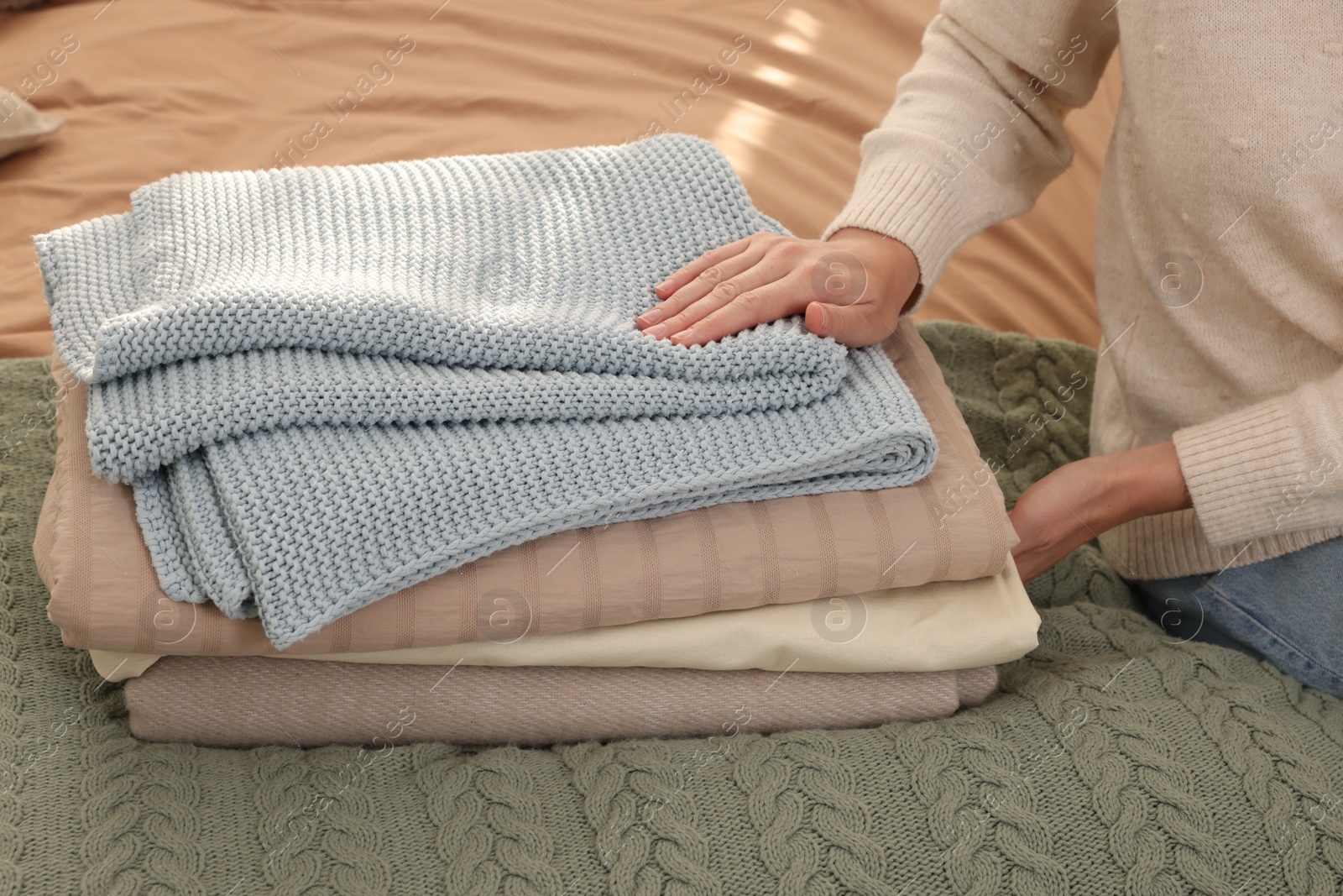 Photo of Woman with stack of different folded blankets on bed, closeup. Home textile