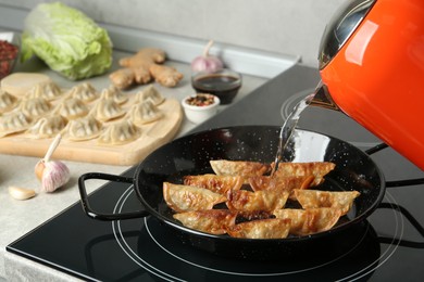 Pouring water on frying pan with gyoza in kitchen