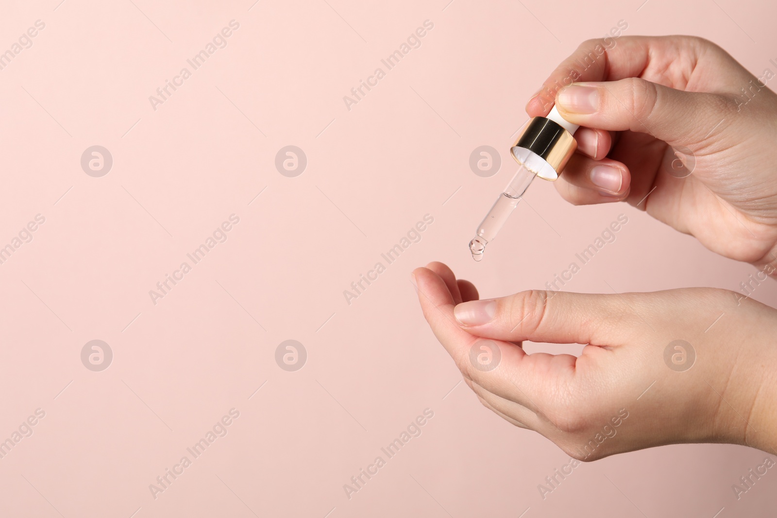 Photo of Woman applying cosmetic serum onto fingers on light pink background, closeup. Space for text