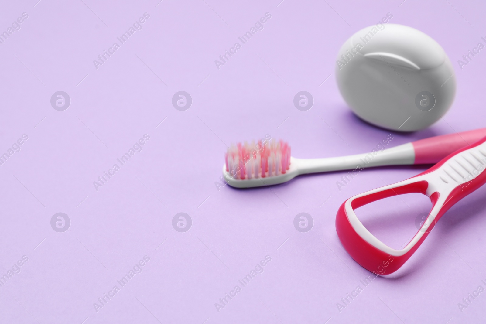 Photo of Red tongue cleaner, toothbrush and dental floss on violet background, closeup. Space for text