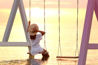 Photo of Young woman enjoying sunrise on swing over water