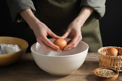 Making bread. Woman adding egg into dough at wooden table on dark background, closeup