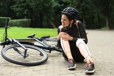 Young woman with injured knee near bicycle outdoors