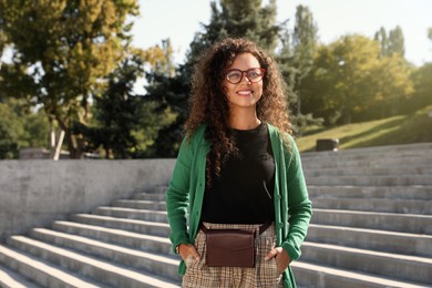 Photo of Beautiful African American woman with stylish waist bag on stairs outdoors