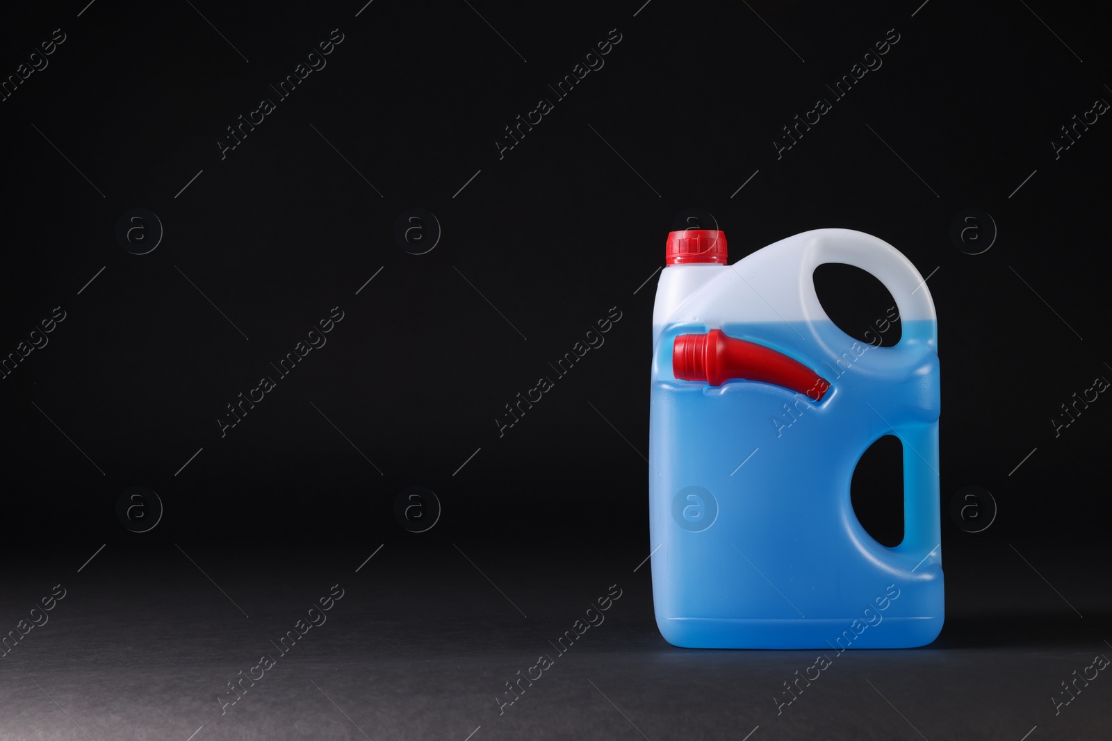 Photo of Plastic canister with blue liquid on black background. Space for text