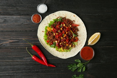 Delicious tortilla with meat on black wooden table, flat lay