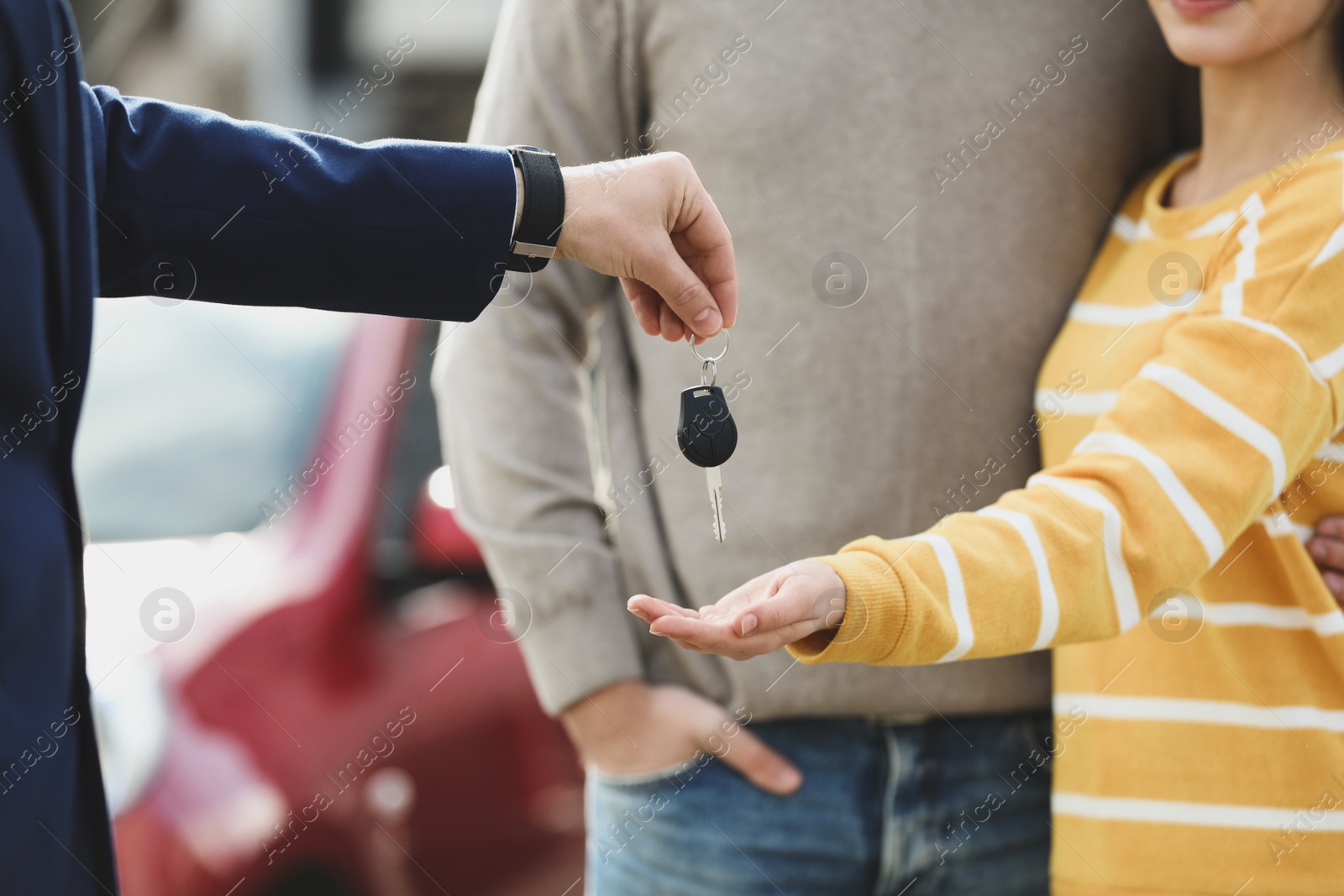 Photo of Salesman giving key to customers in modern auto dealership, closeup. Buying new car