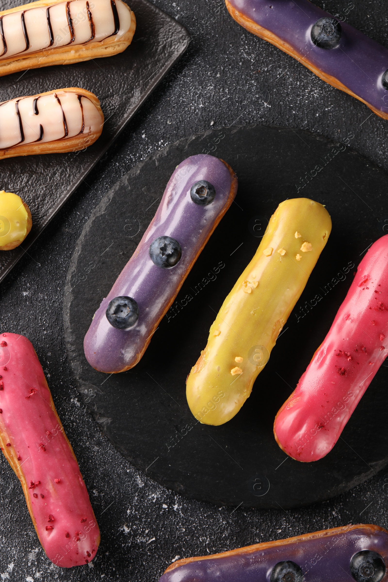 Photo of Different tasty glazed eclairs on dark textured table, flat lay