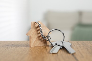 Photo of Keys with keychain in shape of house on wooden table against blurred background, closeup