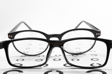 Photo of Vision test chart and different glasses on white background, closeup