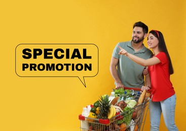 Image of Special promotion. Young couple with shopping cart full of groceries on yellow background