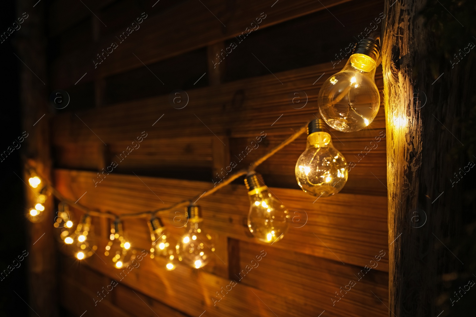 Photo of Garland of lamp bulbs hanging on wooden wall. String lights