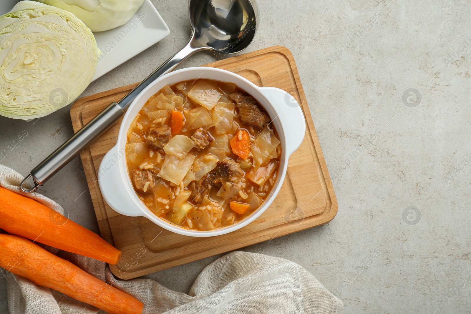 Photo of Tasty cabbage soup and ingredients on light grey textured table, flat lay. Space for text