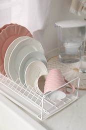 Photo of Drainer with different clean dishware and cup on light table indoors