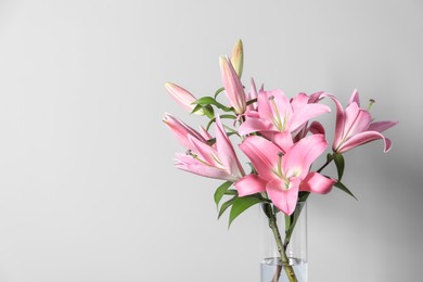 Photo of Beautiful pink lily flowers in vase against light background, space for text