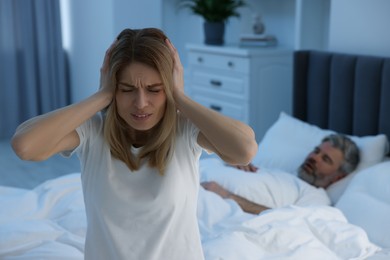 Photo of Irritated woman covering her ears in bed at home, space for text. Problem with snoring husband