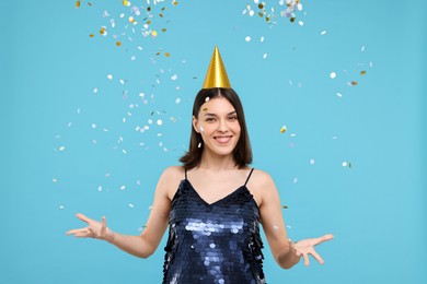 Photo of Happy young woman in party hat near flying confetti on light blue background