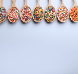 Photo of Colorful sprinkles in spoons on light grey background, flat lay with space for text. Confectionery decor