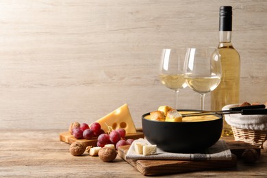 Photo of Tasty cheese fondue, snacks and wine on wooden table, space for text