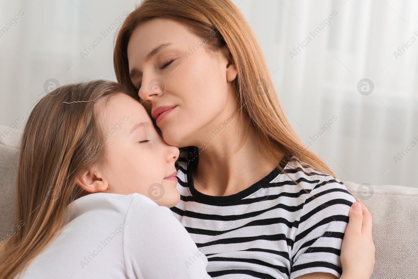 Photo of Mother hugging her cute daughter on sofa at home