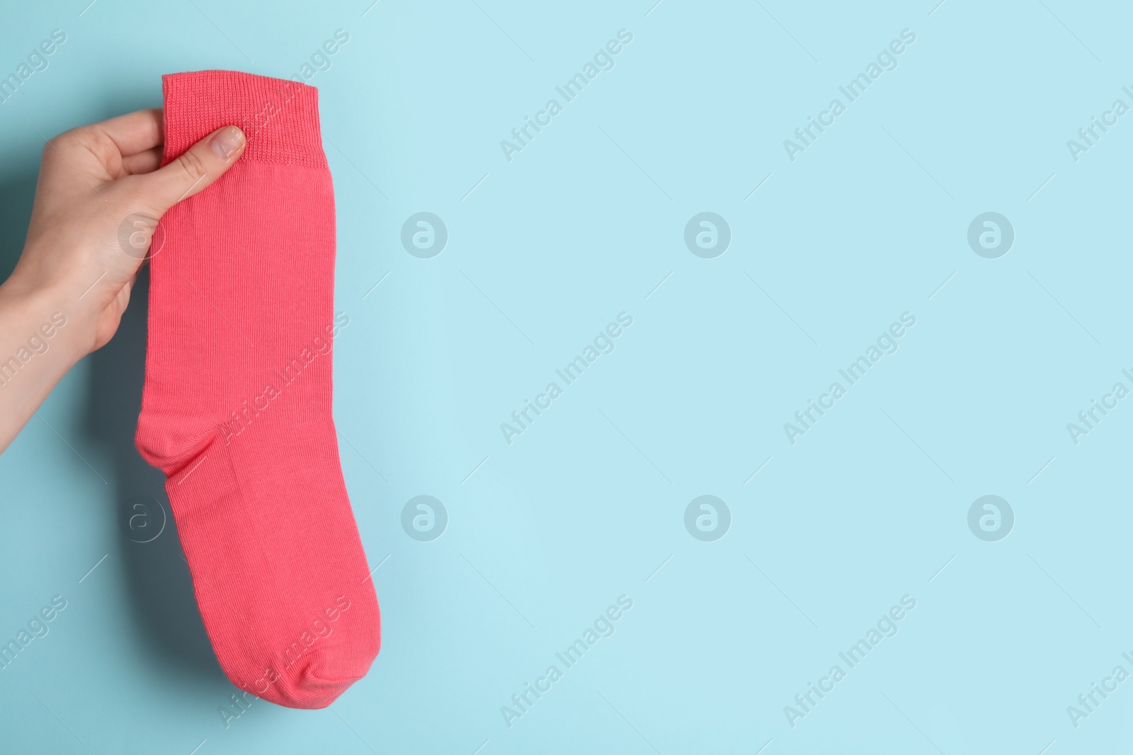 Photo of Woman holding pink sock on light blue background, closeup. Space for text