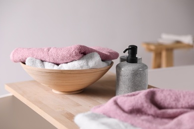 Image of Soap dispenser and folded soft towels on wooden board in bathroom