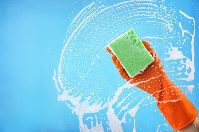 Photo of Woman cleaning glass with sponge against color background