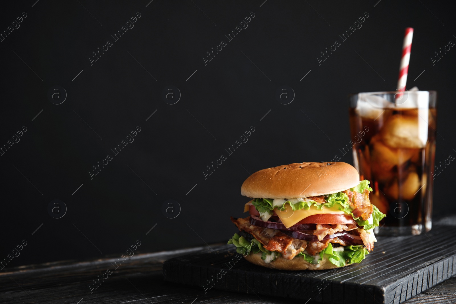 Photo of Tasty burger with bacon and cola on black background. Space for text