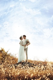 Happy newlyweds with beautiful field bouquet outdoors