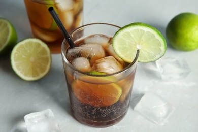 Photo of Glass of cocktail with cola, ice and cut lime on light background