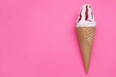 Photo of Delicious ice cream with raspberry jam in waffle cone on pink background, top view. Space for text