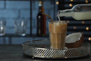 Photo of Pouring syrup into glass of tasty iced coffee on grey table against blurred lights, space for text