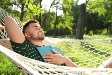 Photo of Young man with book resting in comfortable hammock at green garden