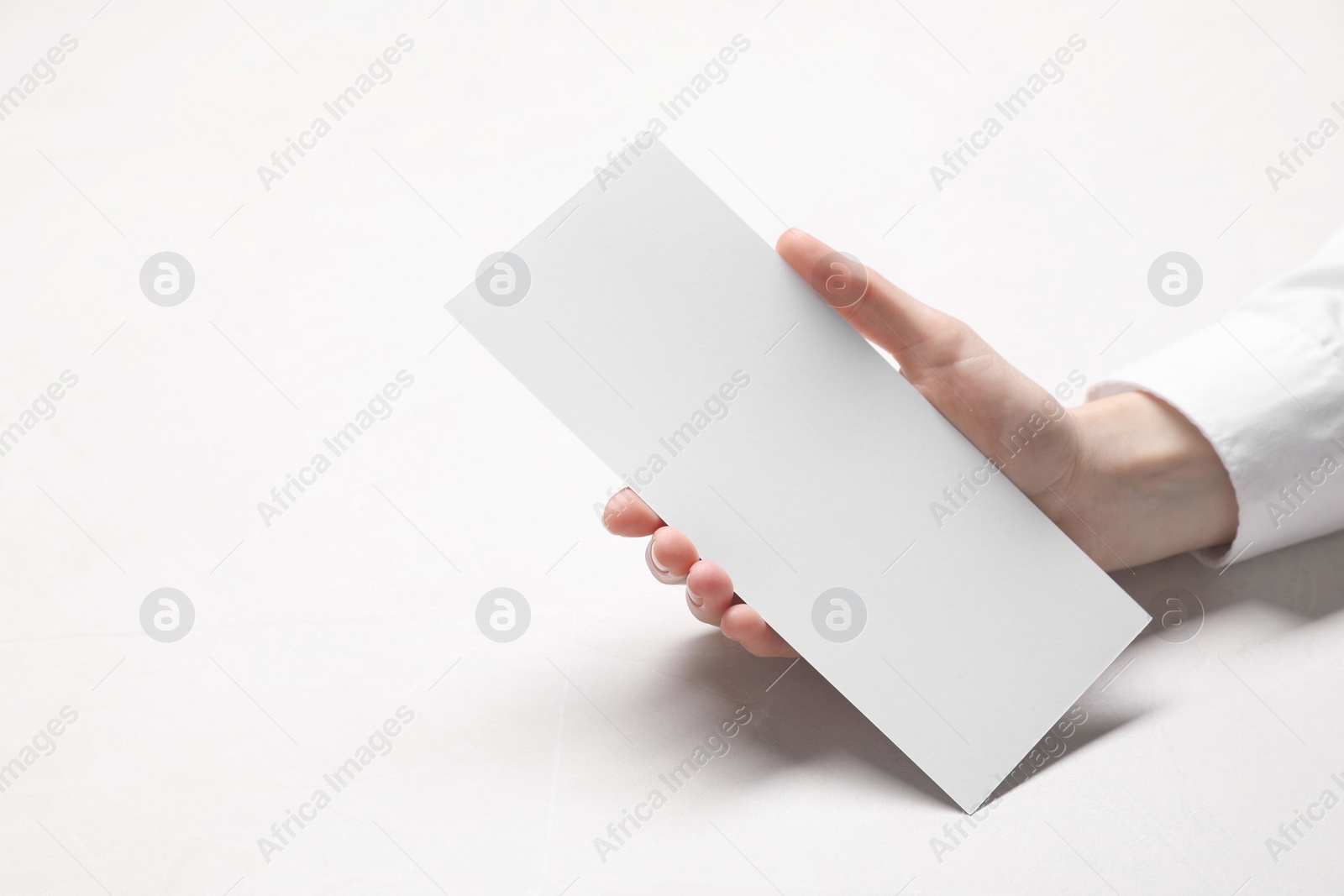 Photo of Woman holding blank card at white table, closeup. Mockup for design