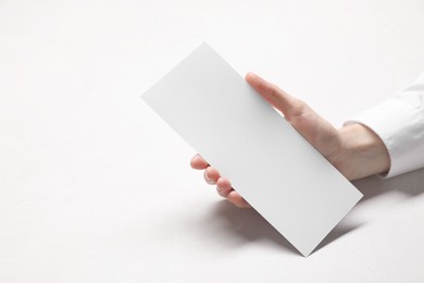 Woman holding blank card at white table, closeup. Mockup for design