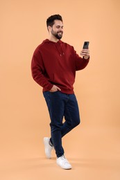 Happy young man using smartphone on beige background