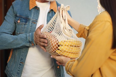 Photo of Helping neighbours. Young woman with net bag of products visiting senior man, closeup