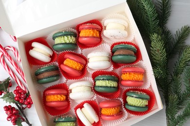 Photo of Different tasty Christmas macarons in box and festive decor on white table, flat lay