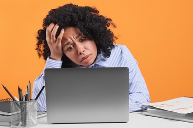 Photo of Stressful deadline. Sad woman looking at laptop at white table on orange background