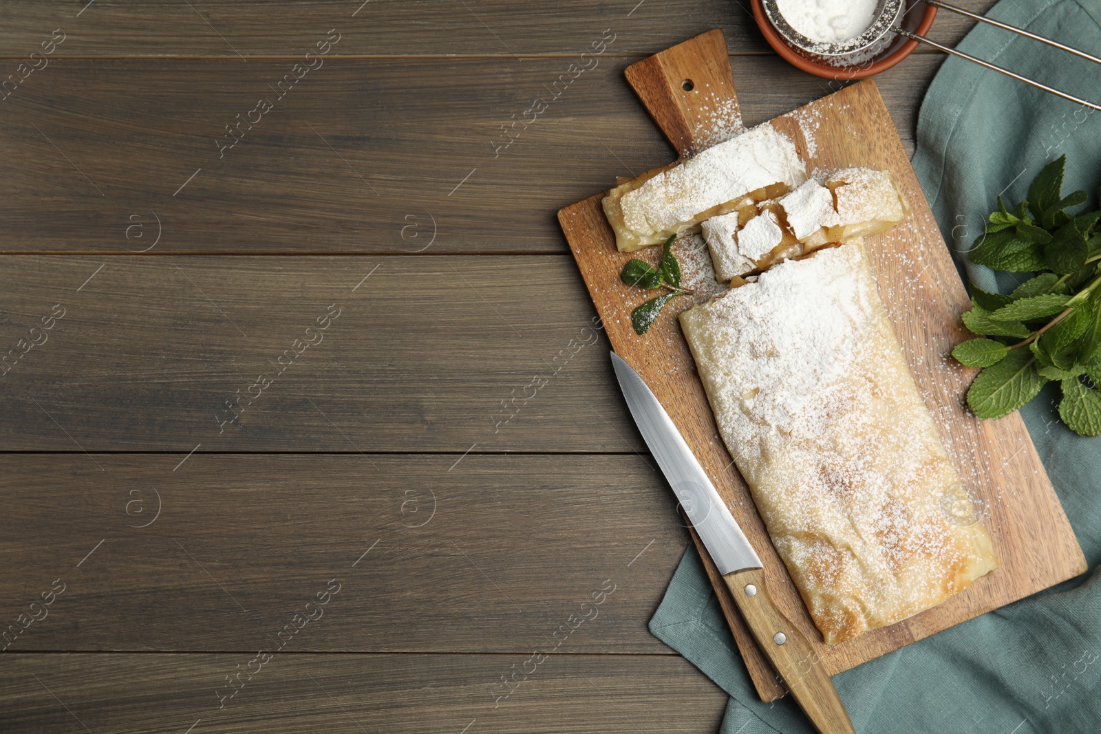 Photo of Delicious apple strudel with powdered sugar and mint on wooden table, flat lay. Space for text