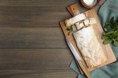 Photo of Delicious apple strudel with powdered sugar and mint on wooden table, flat lay. Space for text