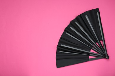 Stylish black hand fan on pink background, top view. Space for text