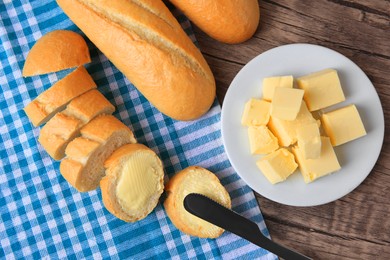 Photo of Tasty cut baguette with fresh butter on wooden table, flat lay